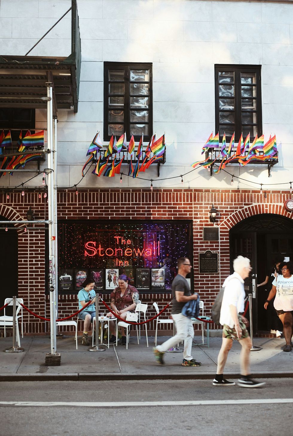 a group of people walking on a sidewalk in front of a the Stonewall Inn in NYC