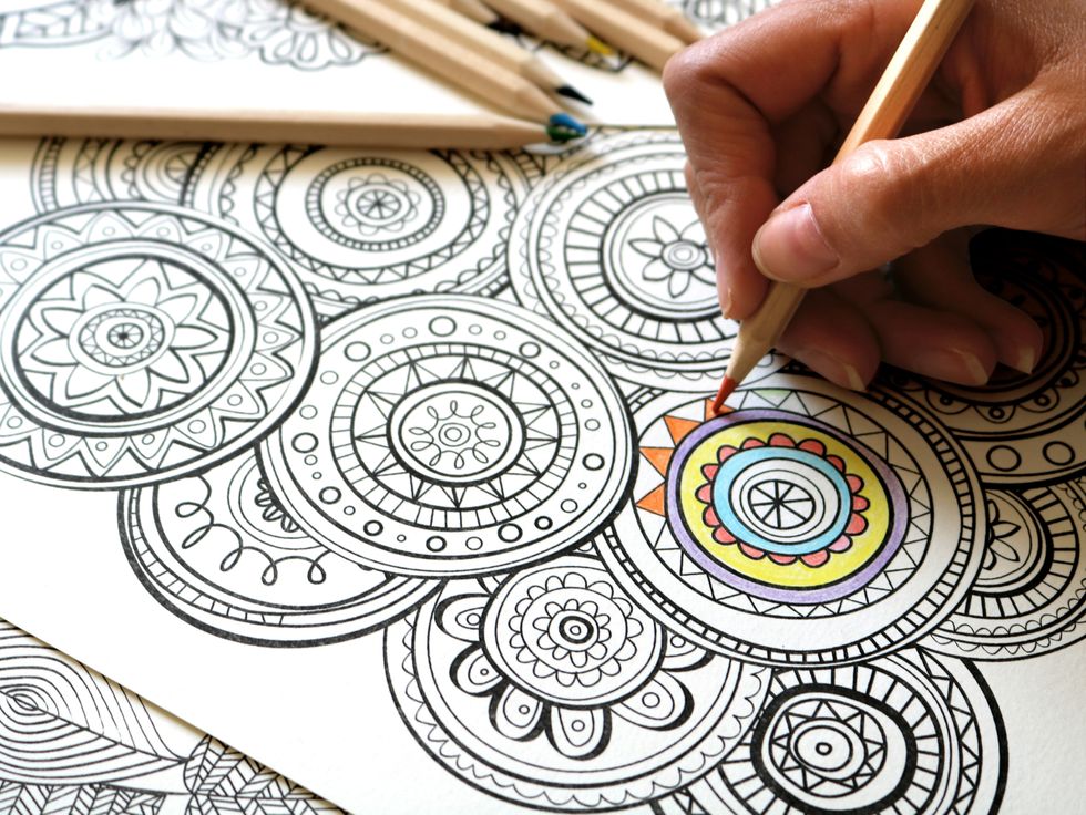 female hand holding colored pencil; coloring a creative and meditative mandala coloring book