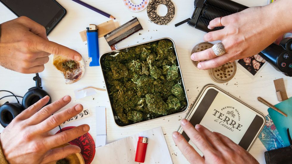 image of a tin of legal cannabis, with several hands preparing it for rolling and consumption