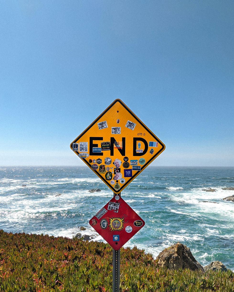 image of California traffic road sign that says - END - at edge of cliff overlooking Pacific Ocean
