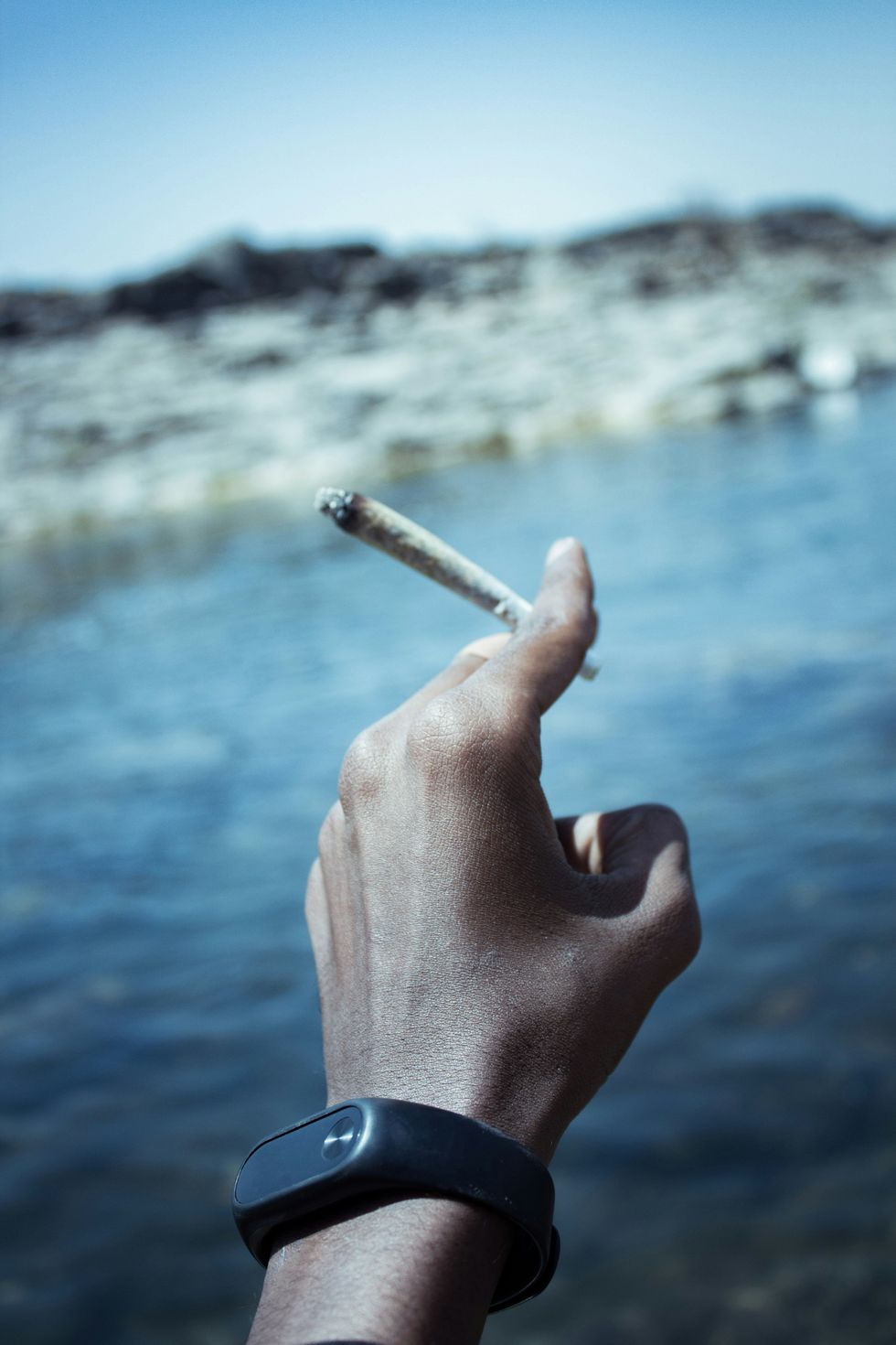 lit pre-roll joint in extended hand wearing a fitbit like device. 
